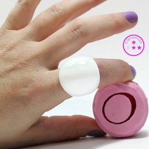 May include: A large, white, round ring is worn on a finger. A pink, geometric-shaped object with a circular indentation is held nearby. The image includes the text "CloneMold" in a circular logo.