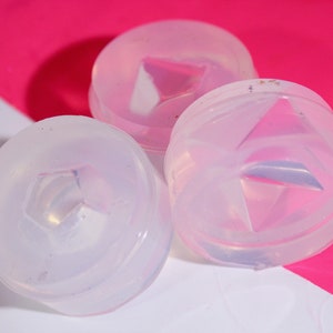 May include: Three clear silicone molds with a raised diamond shape in the center. The molds are round and have a smooth, glossy finish.