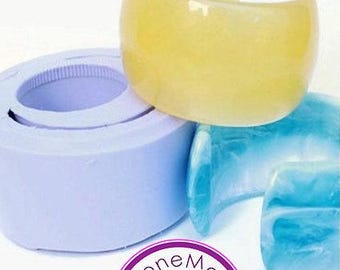 May include: A yellow, translucent cuff bracelet sits atop a light blue bracelet and a purple mold. The cuff is a wide, open design. The image also shows a purple and white logo with the text "CloneMold".