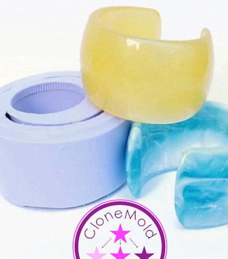 May include: A yellow, translucent cuff bracelet sits atop a light blue bracelet and a purple mold. The cuff is a wide, open design. The image also shows a purple and white logo with the text "CloneMold".
