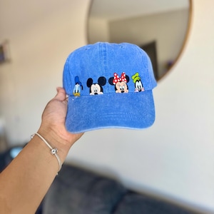 Op de afbeelding: Blauwe baseballcap met geborduurde stripfiguren Donald Duck, Mickey Mouse, Minnie Mouse en Goofy. De cap is effen blauw van kleur en heeft een gebogen klep.