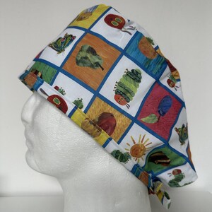 Peut inclure: Un bonnet de chirurgien coloré avec un motif patchwork représentant une chenille, des fruits et des insectes. Le bonnet est en tissu blanc avec une bordure bleue et des liens jaunes.
