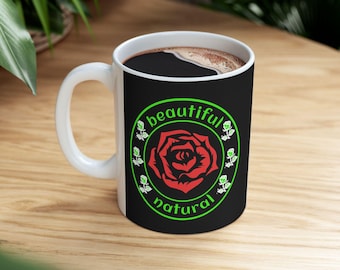 Könnte beinhalten: Weiße Keramik-Kaffeetasse mit einem schwarzen Band, das ein rotes Rosenmuster und die grünen Worte "beautiful natural" zeigt. Die Tasse enthält eine dunkle Flüssigkeit, wahrscheinlich Kaffee oder Tee, und steht auf einer Holzoberfläche.