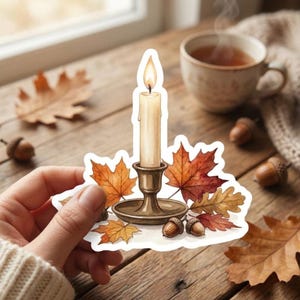 May include: A die-cut sticker featuring a lit cream-colored taper candle in a metallic bronze candlestick holder, surrounded by vibrant orange and red autumn maple leaves and small brown acorns, all set against a white border outline.