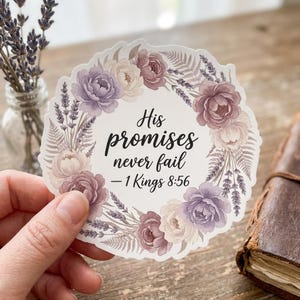 May include: A round sticker with a floral wreath design in shades of purple and cream. The text "His promises never fail - 1 Kings 8:56" is centered within the wreath. The sticker is held by a hand.