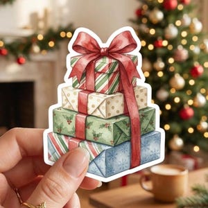 May include: A die-cut sticker featuring a stack of four wrapped gift boxes tied together with a large red ribbon and bow. The boxes have various patterns including red and green stripes, gold polka dots, green holly leaves, and blue snowflakes.