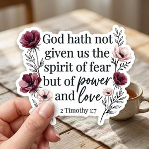 May include: A sticker with the quote "God hath not given us the spirit of fear but of power and love" from 2 Timothy 1:7. The sticker has a white background and is decorated with floral accents in shades of burgundy and pink.