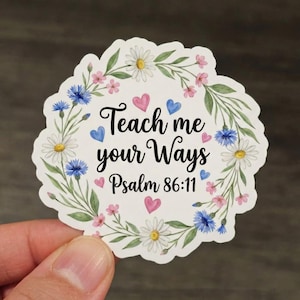 May include: A floral sticker with the text "Teach me your Ways Psalm 86:11". The sticker features a white background with a border of daisies, pink flowers, blue flowers, and green leaves. Pink and blue hearts are scattered around the text.