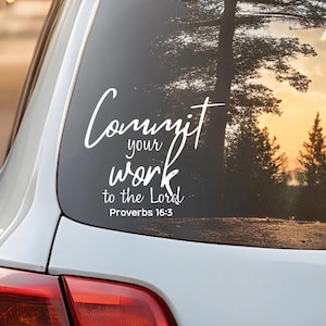 May include: White decal applied to a car window, featuring the script "Commit your work to the Lord" and the reference "Proverbs 16:3". The background shows a sunset through trees.