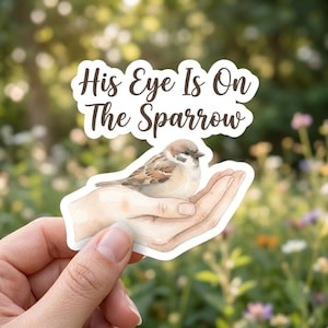 May include: A die-cut sticker featuring a watercolor illustration of a small brown sparrow resting in a pair of open hands. Above the bird, the text "His Eye Is On The Sparrow" is written in a dark brown, elegant cursive script font.
