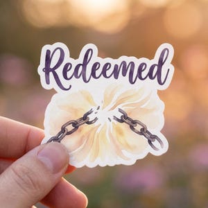 May include: A sticker with the word "Redeemed" in purple script. The sticker features a watercolor design of a flower with a broken chain. The flower is yellow and white.