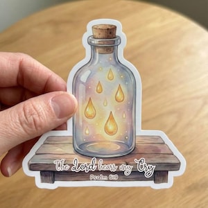 May include: A sticker featuring a clear glass bottle with a cork stopper, containing glowing yellow teardrops. The bottle sits on a wooden surface, with the text "The Lord hears my Cry" and "Psalm 6:9".