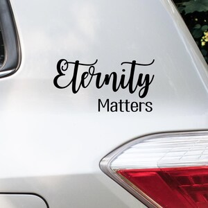 May include: Black vinyl decal with the words "Eternity Matters" in a cursive font. The decal is affixed to the white surface of a vehicle, near the taillight.