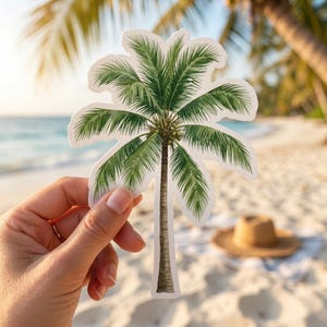 May include: A die-cut sticker featuring a detailed illustration of a palm tree with green fronds and small brown coconuts clustered near the top of the textured brown trunk, outlined with a thin white border against a blurred beach background.