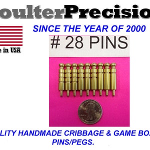 Peut inclure: Ensemble de 28 pions de cribbage en métal doré sur une surface rose. Les pions sont à peu près de la taille d'une pièce de 25 cents américaine. Le texte "#28 PINS" est visible sur une carte blanche.