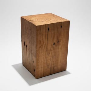May include: A solid, rectangular wooden block with a natural wood grain finish. The block is a warm brown color and has visible knots and imperfections, suggesting it is made from reclaimed wood. The block's dimensions are approximately 12 inches tall, 10 inches wide, and 10 inches deep.