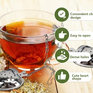 May include: A glass teacup filled with amber tea, with a heart-shaped stainless steel tea infuser. The infuser is attached to a chain and hook. The image also shows chamomile flowers and text that says "Convenient chain design", "Easy to open", "Dense holes", and "Cute heart shape".