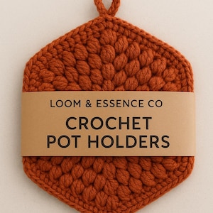 Könnte beinhalten: Sechseckiger, rostfarbener Topflappen aus Häkelarbeit mit einer Schlaufe zum Aufhängen. Der Topflappen hat ein strukturiertes, erhabenes Muster. Ein braunes Papierband in der Mitte trägt die Aufschrift "LOOM & ESSENCE CO CROCHET POT HOLDERS."