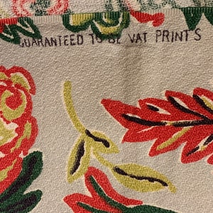 Peut inclure: Gros plan sur un tissu blanc avec un motif floral dans les tons de rouge, vert et jaune. Le tissu a une surface textur&eacute;e et le texte "GUARANTEED TO BE VAT PRINTS" est visible en haut.