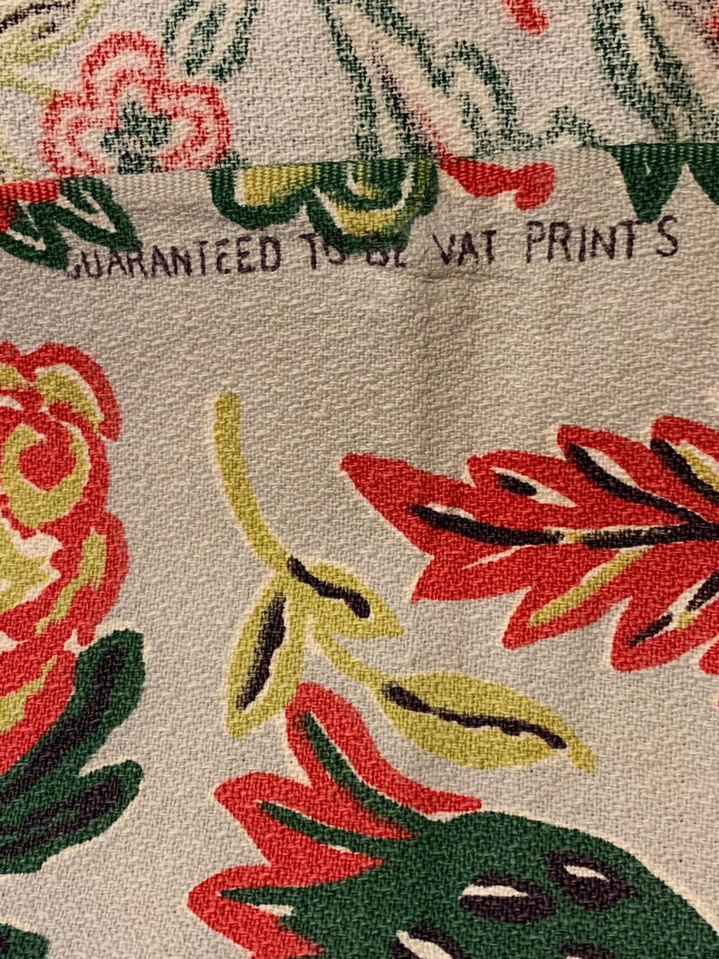 Peut inclure: Gros plan sur un tissu blanc avec un motif floral dans les tons de rouge, vert et jaune. Le tissu a une surface textur&eacute;e et le texte "GUARANTEED TO BE VAT PRINTS" est visible en haut.