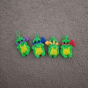 May include: Four small green rubber band figures of the Teenage Mutant Ninja Turtles. Each figure has a different coloured mask and bandana. The figures are arranged in a row on a brown fuzzy surface.