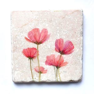 Könnte beinhalten: Ein quadratischer, cremefarbener Steinuntersetzer mit einem Aquarellgemälde von rosa Kosmosblumen. Die Blumen haben zarte Blütenblätter und schlanke grüne Stiele. Der Untersetzer hat eine strukturierte Oberfläche.