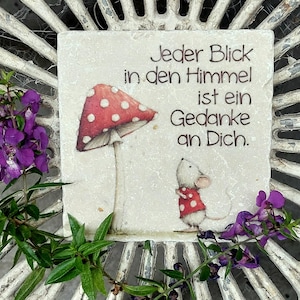 Könnte beinhalten: Eine quadratische Steinplatte mit einem rot-weiß gepunkteten Fliegenpilz und einer kleinen weißen Maus in einem rot-weiß gepunkteten Hemd. Der Text lautet: Jeder Blick in den Himmel ist ein Gedanke an Dich. Die Platte hat eine strukturierte, cremeweiße Oberfläche.
