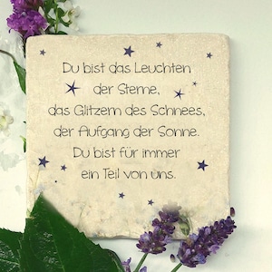 Könnte beinhalten: Ein quadratischer, cremeweißer Stein mit dunkelviolettem Text: Du bist das Leuchten der Sterne, der Glitzern des Schnees, der Aufgang der Sonne. Du bist für immer ein Teil von uns. Der Stein ist mit kleinen violetten Sternen verziert.
