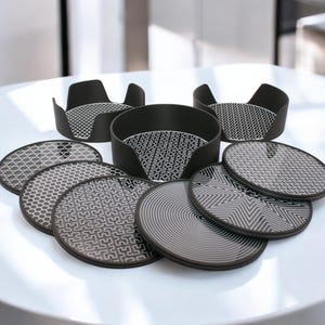 Könnte beinhalten: Satz mit acht Untersetzern mit schwarz-weißem Muster. Die Untersetzer sind rund und haben verschiedene geometrische Designs. Die Untersetzer sind auf einem weißen Tisch in einem Kreis angeordnet.