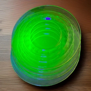 May include: A stack of translucent, circular, neon green glass plates. The plates are layered on top of each other, creating a concentric ring pattern with a vibrant, glowing appearance. The edges of the plates are smooth and rounded.