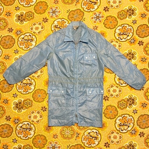May include: A light blue vintage jacket with a zip-up front, collared neckline, and multiple pockets. The jacket has a cinched waist and long sleeves. The background is a yellow floral pattern.
