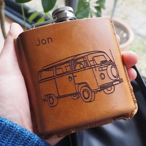 K&ouml;nnte beinhalten: Eine braune Lederflasche mit silbernem Verschluss und einer personalisierten Gravur mit dem Text "Jon". Die Flasche zeigt ein eingegraveertes Design eines alten Volkswagen-Transporters.