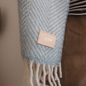 May include: A blue and white chevron patterned scarf with a brown leather tag that says "MUM" on it.