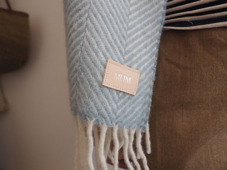 May include: A blue and white chevron patterned scarf with a brown leather tag that says "MUM" on it.