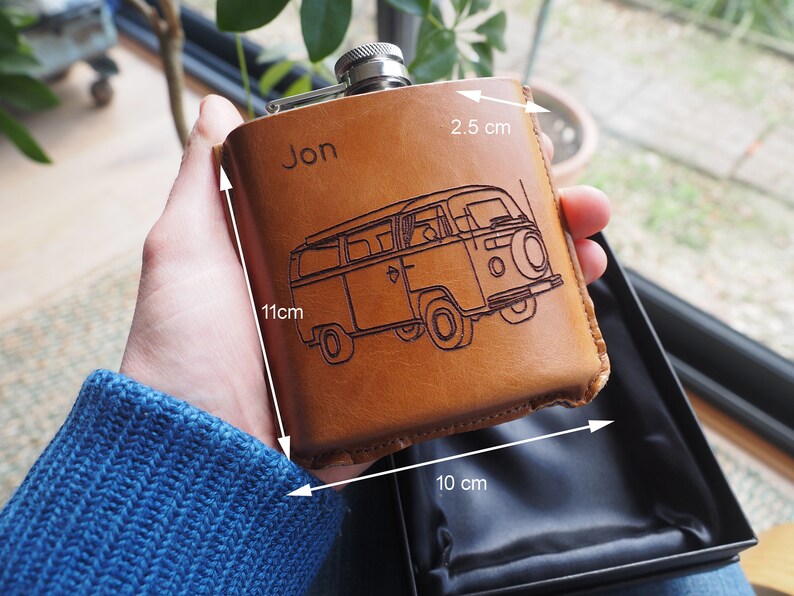 K&ouml;nnte beinhalten: Eine braune Lederflasche mit einer personalisierten Gravur "Jon" und einem eingegrabenen Bild eines Vintage-Vans. Die Flasche ist 11 cm hoch, 10 cm breit und 2,5 cm tief.