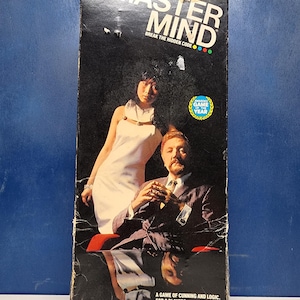 May include: A vintage "Master Mind" board game box with a black background. The box features the game's title in white and a graphic of a man and woman. Text on the box reads "A game of cunning and logic" and "Ages 8 to adult."