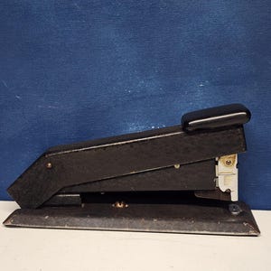 May include: A black metal stapler with a textured finish and a black plastic handle. The stapler has a silver metal staple loading mechanism.