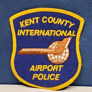 May include: A blue and yellow embroidered patch with the text "Kent County International Airport Police".