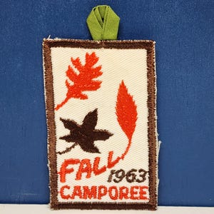May include: Rectangular patch with a cream background, brown border, and green ribbon. Features orange and brown leaf designs and the words "FALL CAMPOREE 1963" in orange and brown.