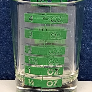 May include: A clear glass measuring cup with green markings for 1/2, 1, 1 1/2, 2, 3, and 4 ounces.