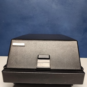 May include: A black vintage Polaroid camera with a silver nameplate and a black plastic lens cover.