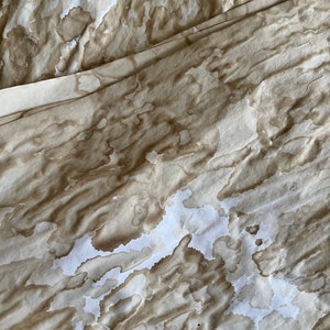 May include: A close-up of a white fabric with brown stains, creating a mottled, abstract pattern.