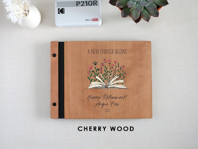A wooden binder with a floral design and text, placed on a white surface next to a small white object and a potted plant.