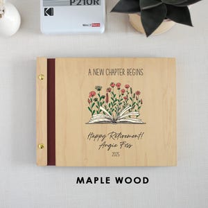 A wooden binder with a floral design and text, placed on a table next to a white vase and a small plant.