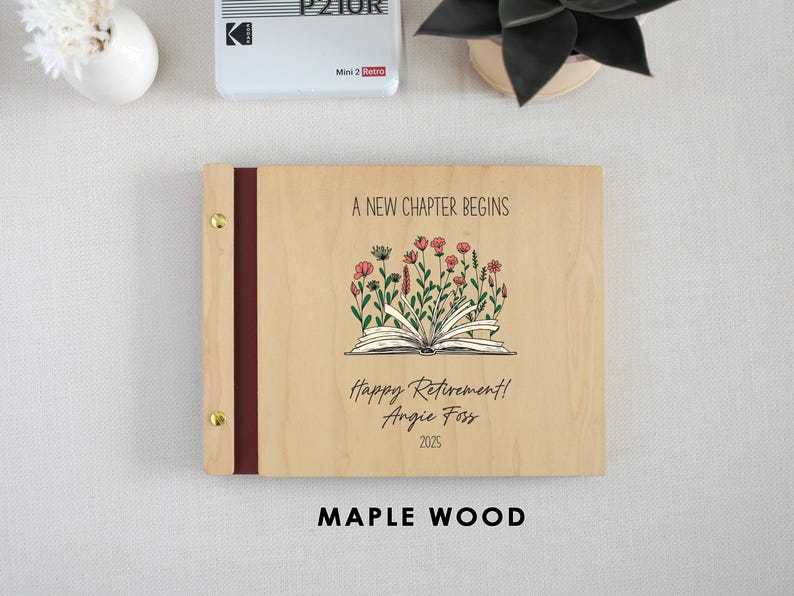 A wooden binder with a floral design and text, placed on a table next to a white vase and a small plant.