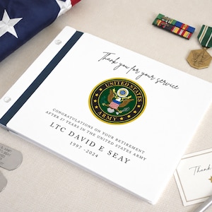 May include: A white retirement book featuring the United States Army emblem, the text "Thank you for your service," "CONGRATULATIONS ON YOUR RETIREMENT AFTER 27 YEARS IN THE UNITED STATES ARMY," "LTC DAVID E SEAY," and "1997 - 2024" with metal tags.