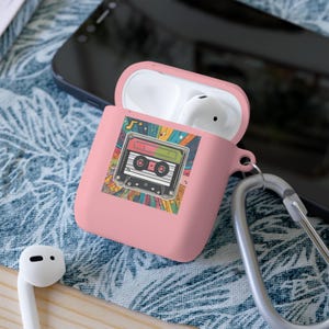 Op de afbeelding: Roze Airpods-hoes met een kleurrijk retro-cassettebandontwerp. De hoes heeft een zilveren karabijnhaak.