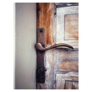 May include: A brass door handle with a curved lever and a keyhole on a weathered wooden door.