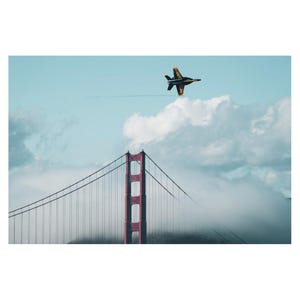 May include: A black and yellow fighter jet flies over the Golden Gate Bridge in San Francisco, California. The bridge is partially obscured by fog.