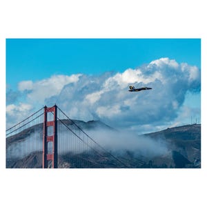 May include: A red bridge with a blue and yellow airplane flying over it. The bridge is partially obscured by fog and clouds.